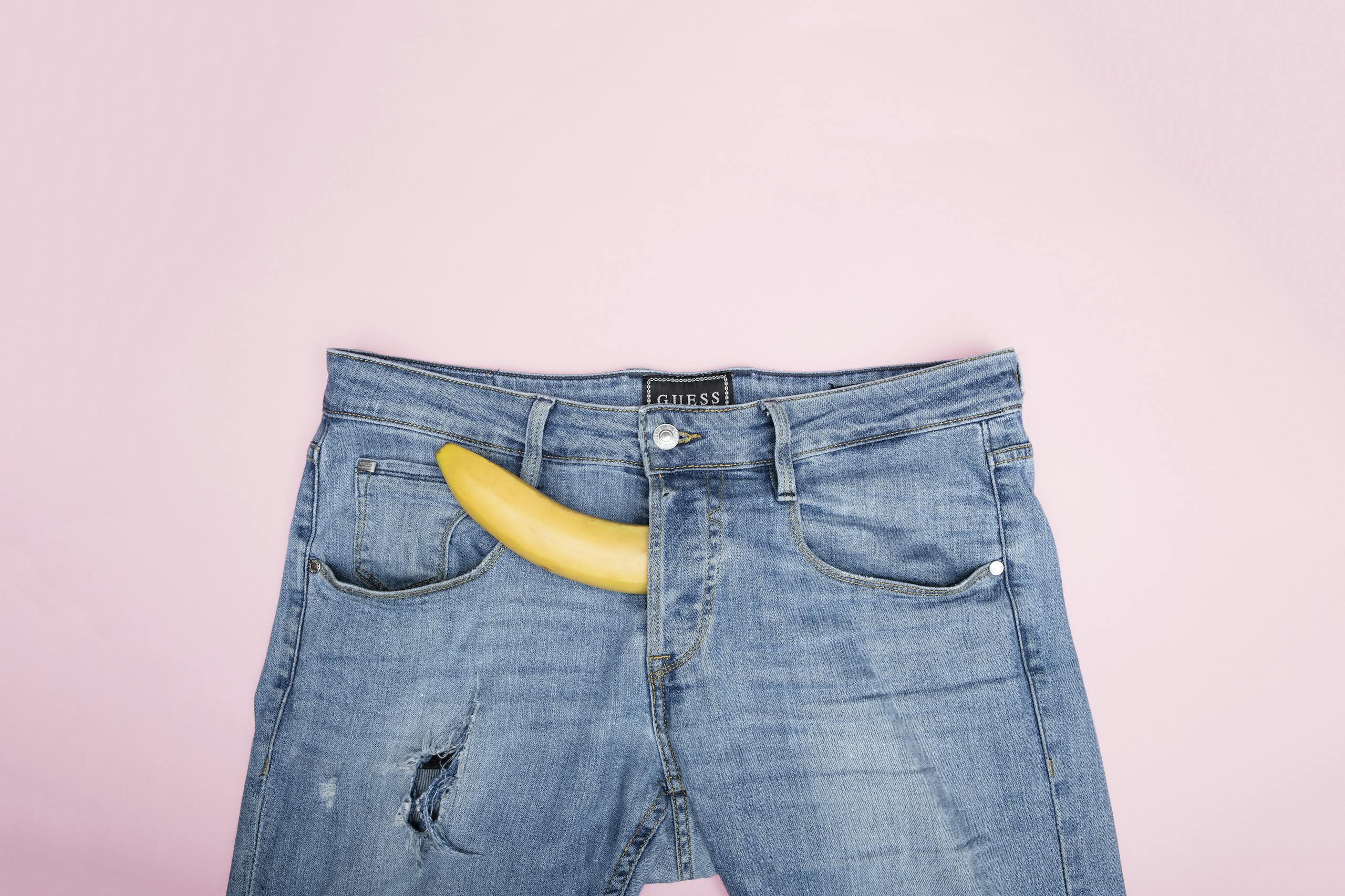 Fun and conceptual still life photo featuring a banana in blue jeans against a pink background.