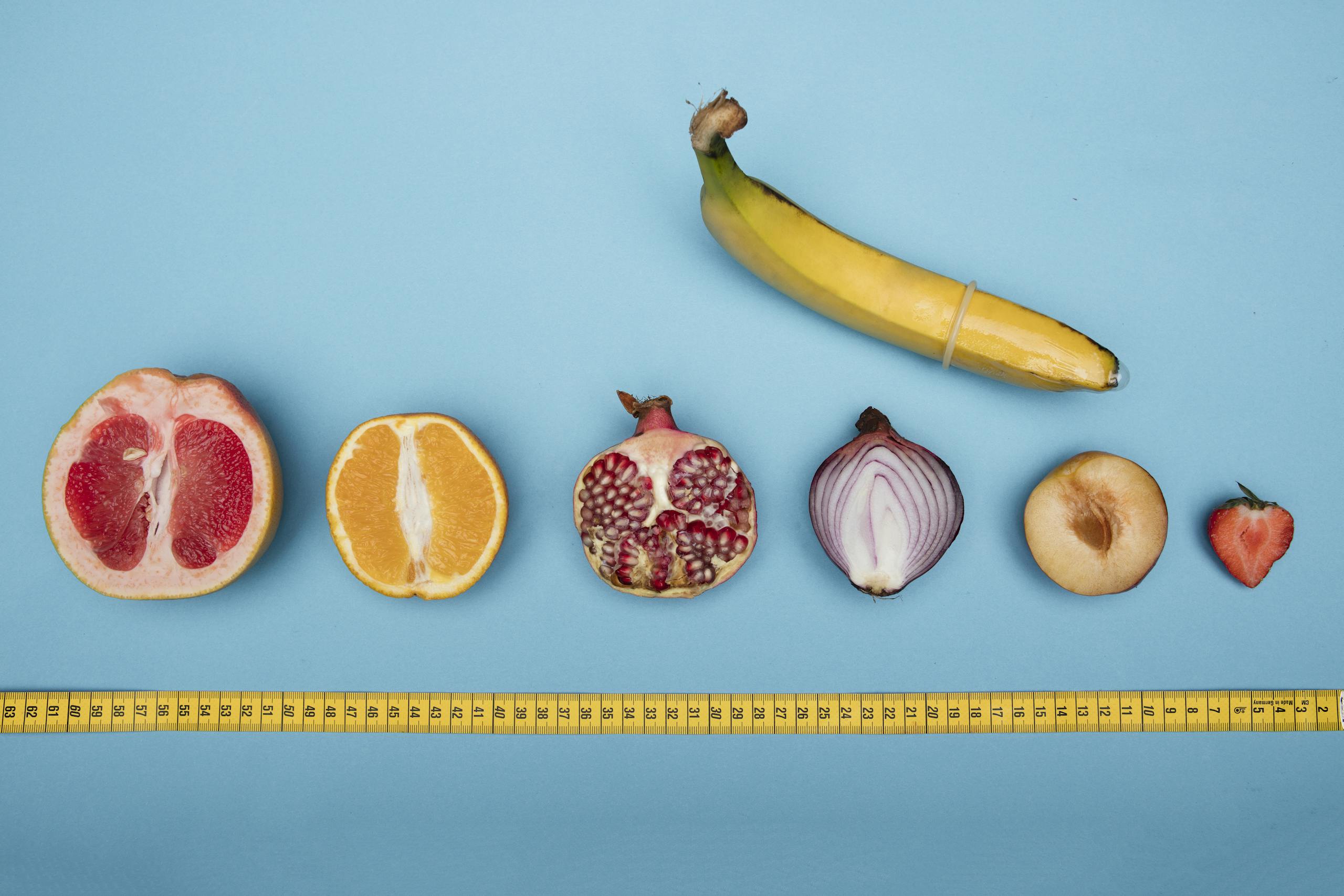 Humorous arrangement of fruits and a banana with condom on blue background.